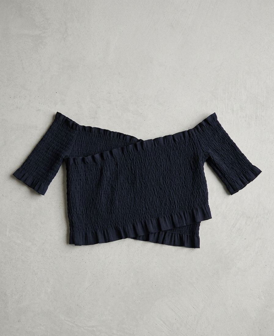 Crop top negro de hombros descubiertos, mangas cortas y un diseño totalmente confeccionado en nido de abeja con extremos asimétricos cruzados